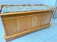 front view of light oak storage bench showing floral painted panels and tapestry seat