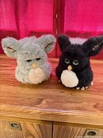 Front view of both gray and black Furby toys on wooden surface