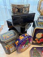 Group of tins showing oval floral, black stack, Bassett's, Disney round, floral bouquet, other tins