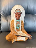 Front view of multicolor plaster figurine seated holding pipe
