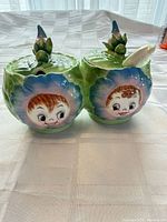 Pair of closed condiment pots with lids and spoon visible