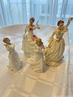 Group of four Royal Doulton Victorian lady figurines displayed on table