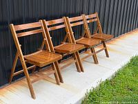 Four wooden folding chairs lined against wall, side view