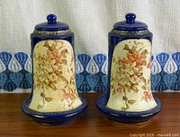 Front view of both cobalt flow blue lidded vases with floral panels