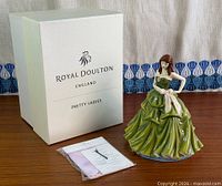 Front view of figurine beside branded box and leaflet