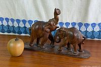 Front view of two-elephant wooden sculpture on base with scale reference apple