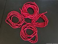 Five coiled red wooden bead garlands displayed on black surface