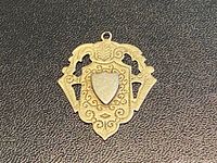 Front view of ornate sterling silver watch fob medal with blank gold-accented shield