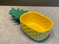 Angled view of yellow pineapple ceramic bowl with green crown handle
