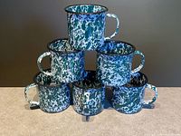 Six green and white splatter enamel mugs stacked pyramid style showing pattern and black rims