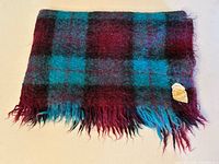 Folded blanket showing plaid pattern and fringe, original label visible