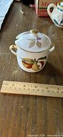 Porcelain condiment jar with lid, handles and fruit design beside ruler
