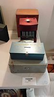 All three items side by side: gray cash box, blue ticket box, red SunHill coin sorter