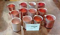 Top view of eleven copper-rose aluminum mugs with handles arranged on table