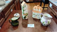 Five Countryman Ceramics pieces displayed on countertop: rose pitcher, green creamer, two house-form containers, round floral trinket box