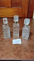 Front view of three clear cut glass square decanters with faceted stoppers showcasing pattern and condition