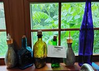 Group shot of six decorative glass bottles on windowsill, various colours and tops visible