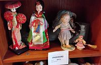 Shelf with two Asian dolls, bisque toddler, miniature broom doll, and grey reading statue