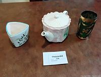 Overview of three items on table: triangular planter, relief teapot, gilt glass vase