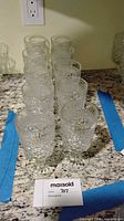 Top angled view of all 12 clear pressed diamond pattern goblets arranged in rows on countertop