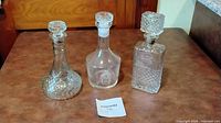 Group shot of three clear glass decanters with stoppers