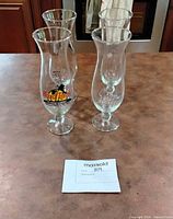 Four hurricane glasses grouped on countertop showing branded and plain pieces