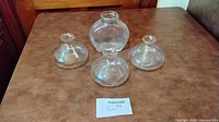 Four clear glass lamp chimneys arranged on tabletop showing overall shape and condition