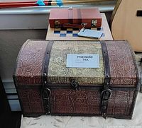 Closed embossed chest and smaller suitcase-style game case atop table
