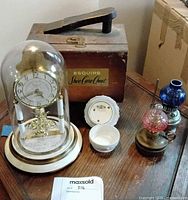 Group view: Esquire chest, anniversary clock under glass dome, two miniature oil lamps, porcelain dishes