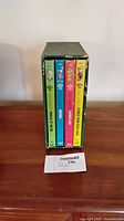 Front view of four hardcover volumes in worn green slipcase, showing spine titles and colours