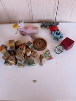 Group shot of all items including pull duck, blocks, spinning top, gyroscope, whistle, marbles, locomotive, tea set pieces