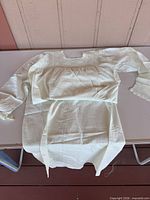 Full view of white cotton nightgown laid flat showing crocheted lace yoke, sleeves, cuffs, and hem