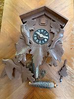 Front view of cuckoo clock body showing carvings, dial and detached parts