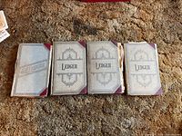 Four antique ledgers laid side by side showing covers