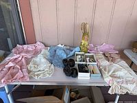 Overview of table with vintage baby clothes, shoes, grooming items, stuffed bunny