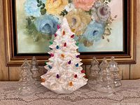Front view of ceramic Christmas tree illuminated with multicolour pegs, flanked by six clear glass tree containers