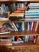 Three shelves filled with assorted hardcover and paperback books, various titles visible