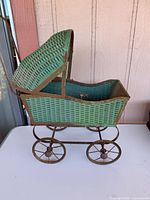 Full left side view of green wicker doll carriage showing wheels and canopy
