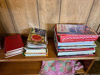 Two stacks of cookbooks on wooden shelf showing quantity and variety