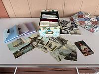 Lot overview showing storage box, loose postcards, black-and-white photos, three mini folders