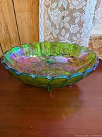 Oblong green iridescent carnival glass bowl on wooden surface showing scalloped rim and tri-footed base