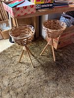 Two woven wood tripod planters standing on carpet