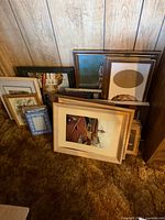 Stack of assorted frames leaning against wood panel wall