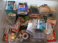 Overview of bin showing packaged E-Z Ancor anchors, Tapcon screws, Master Plumber items, hose clamp, PTFE tape and assorted hardware