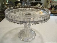 Full view of clear pressed glass pedestal cake stand with bullseye pattern and scalloped edge