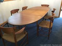 Full view of extended oval teak dining table with all six chairs arranged around it.