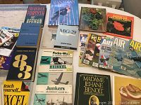 Various books and magazines laid out on a wooden floor, including titles on birds, aircraft, houseplants, and cooking.