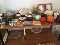 Front view of wooden shelves with assorted candles, candle holders, decorative plates, coasters, tins, lace cloths.