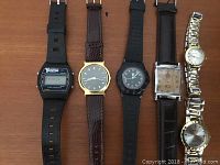 Top-down view showing all six watches laid side by side on a wooden surface displaying bands and faces.