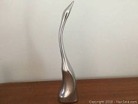 Full view of the aluminum sculpture showing its abstract streamlined shape and smooth surface.